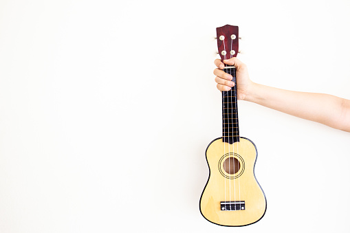 Women's hand holds the classic Ukulele close up with copy space in left side.