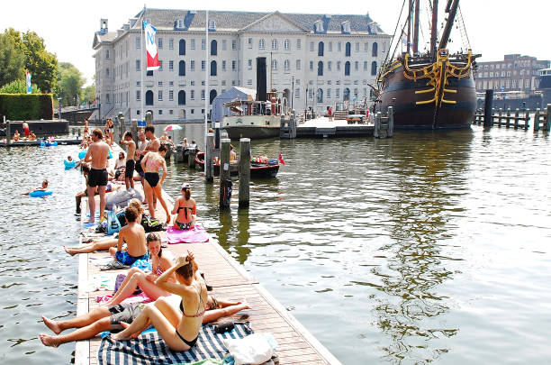 Young people swimming and enjoying the sun on the new floating boardwalk constructed across the inner harbor of the navy pier 'Marineterrein'in Amsterdam. This platform was built in 2018 and has created a beautiful walking route for walkers and a new space for swimmers. At the background of the picture is seen the National Maritime Museum of the Netherlands known as \