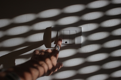 Close up on woman hand on light switch with morning shadows from blinds