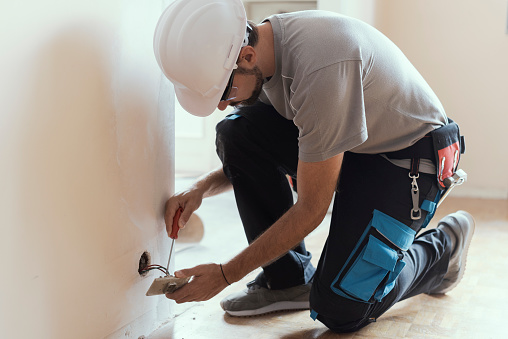 Professional electrician installing sockets using a screwdriver: home renovation and maintenance concept