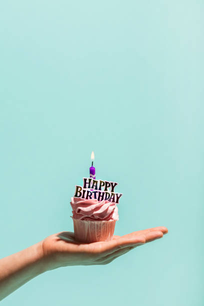 istock Woman's hand holding birthday cupcake with candle. 1060939442