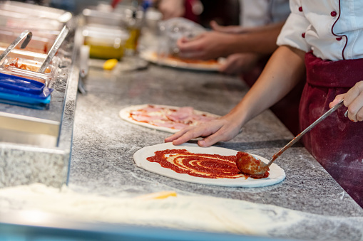 Mid section of chef using ladle to spread sauce on a pizza