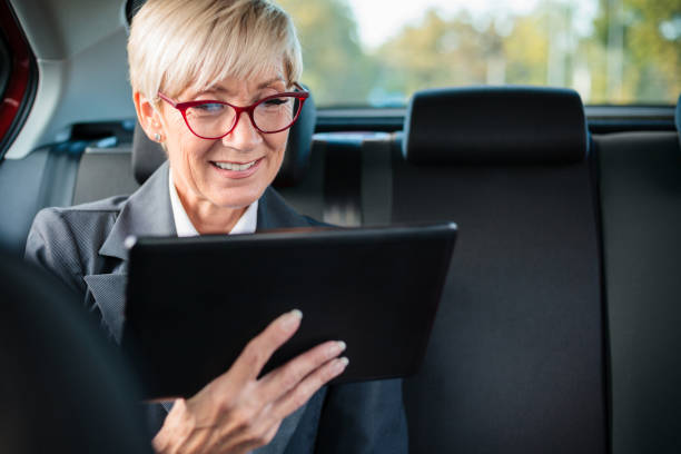 felice imprenditrice matura sorridente e usando il tablet su un sedile posteriore dell'auto - taxi travel business women foto e immagini stock