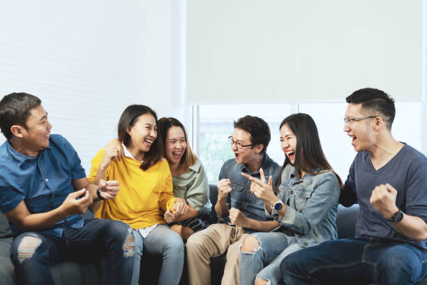 séduisante jeune asiatique entre amis parler et rire avec les heureux en séance de la réunion de rencontre à la maison, se sentant gaie et profiter ensemble de jeu en temps de loisir. personnes portant des bleus ou jaunes. - humor men laughing teenager photos et images de collection