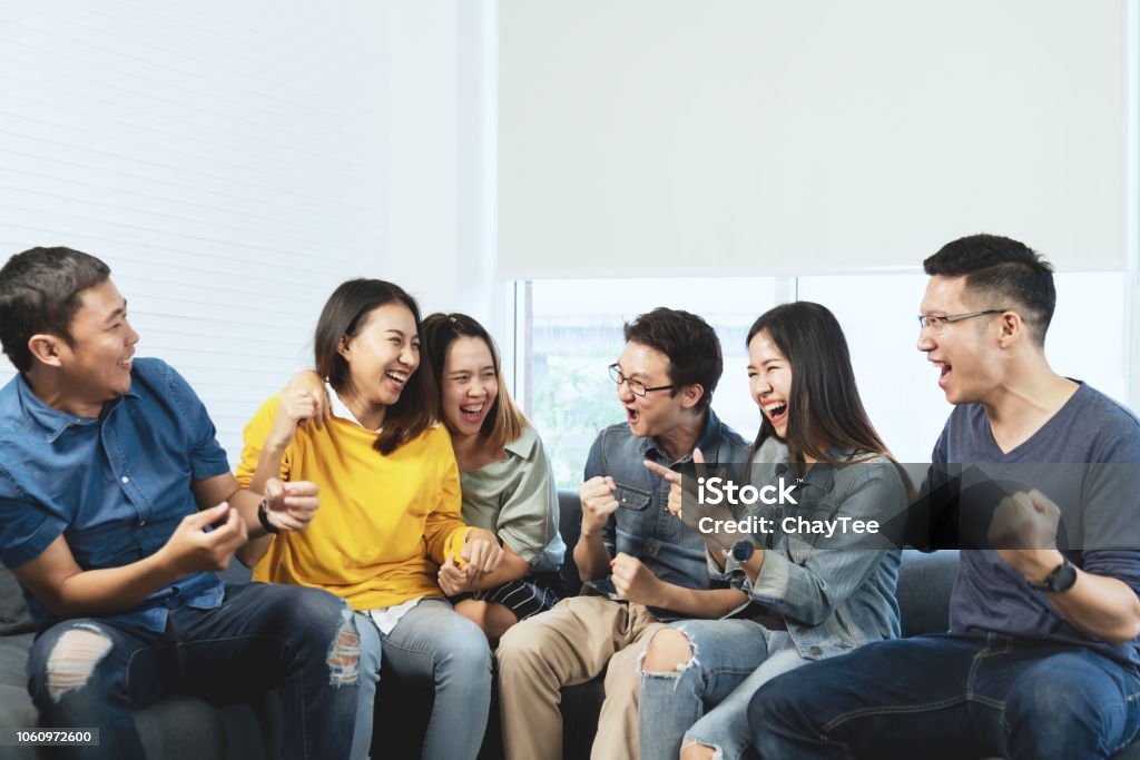 Young Attractive asian group of friends talking and laughing with happy in gathering meeting sitting at home feeling cheerful and enjoy game in leisure time together. People in blue or yellow wearing. Asia Stock Photo