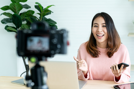 Joven mujer asiática atractiva blogger o vlogger mirando a cámara y hablar sobre la toma video con tecnología. Los medios de comunicación social influyente personas o contenido creador concepto en relax estilo casual en el hogar. photo