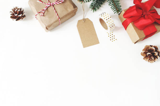 Christmas composition. Frame of fir tree branches, pine cones, christmas gift boxes, tag, golden washi tape, ribbons on white table background. Traditional still life arrangement. Flat lay, top view.