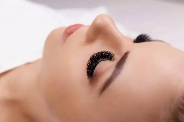 Photo of Eyelash Extension Procedure. Woman Eye with Long Eyelashes. Close up, selective focus. Fashion, russian volume