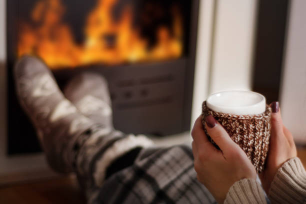 Girl drinking hot tea in front of the fireplace and warming legs stock photo