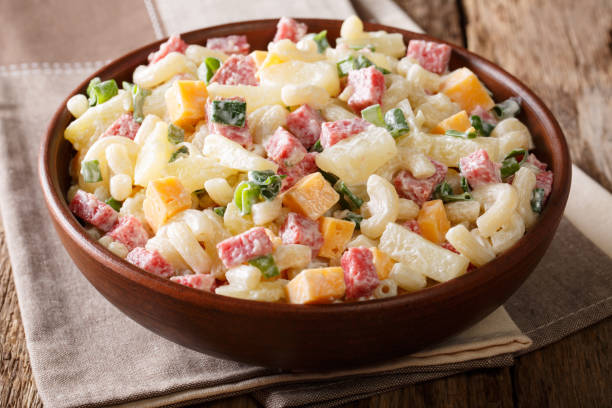 istock Hawaiian cuisine: salad with pasta, ham, pineapple, onion, cheddar cheese with mayonnaise close-up. horizontal, rustic style 1060987582