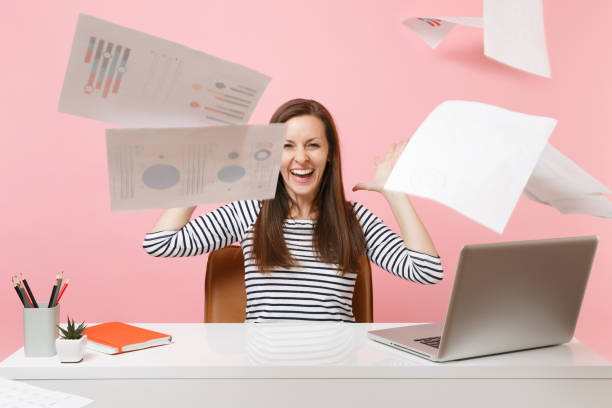istock Young laughing woman throwing up paper documents while working on project, sitting at office with laptop before weekend isolated on pink background. Achievement business career concept. Copy space. 1060991016