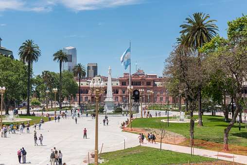 People walking on Plaza de Mayo next to the Pyramid of May (Pirámide de Mayo) right in the center of  the square at downtown Buenos Aires, Argentina. At the background is the Pink House (Casa Rosada), the executive mansion and office of the President of the country. Historically, the pyramid and the plaza are witnesses of all the demonstrations and claims made by the people to their rulers.