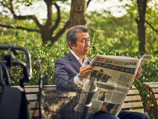A mature Japanese man in a business suit, reading a newspaper in an outdoor setting in Tokyo, Japan.