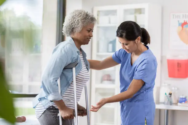 Photo of Senior patient with crutches is helped by young nurse