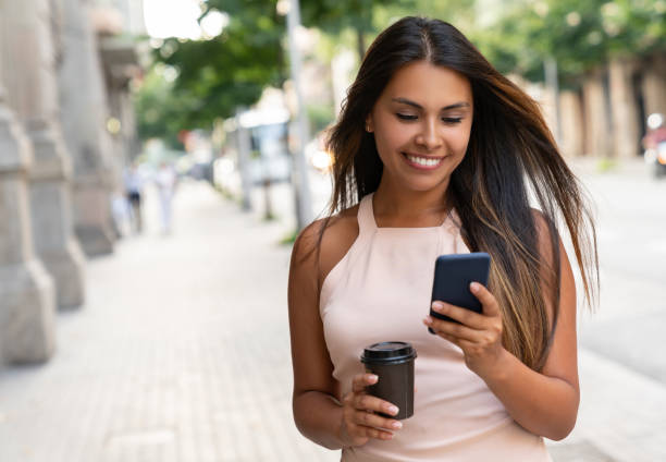 istock Woman using cell phone and drinking coffee on the street 1061002584
