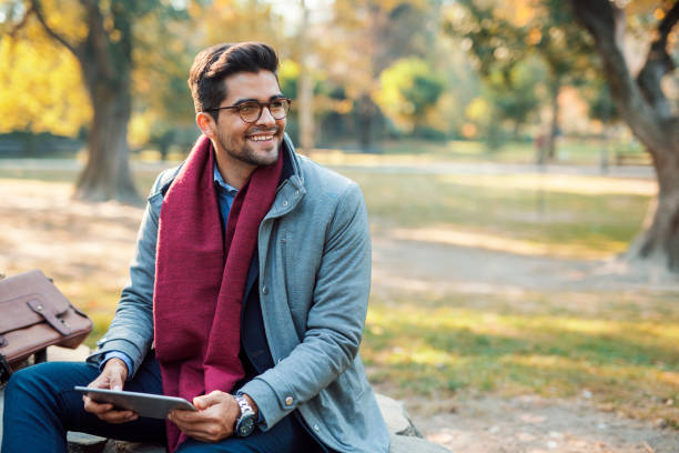 Man using tablet Handsome young businessman reading at public park scarf photos stock pictures, royalty-free photos & images