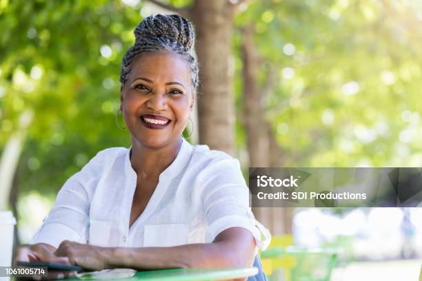 Senior Woman Smiles At The Camera While Sitting In Quiet Park Stock Photo - Download Image Now