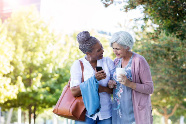 старшие подруги связывают руки во время прогулки на открытом воздухе - grandmother standing senior women senior adult стоковые фото и изображения
