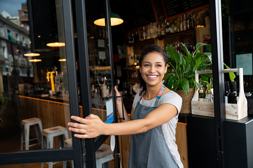 Portrait of a happy business owner opening on the door at a cafe and smiling â small business concepts