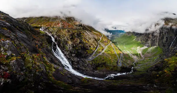 Photo of Aerial Panorama View of Trollstigen Road in Norway with Rushing Waterfall and Mountains and Traffic with Clouds and Fog