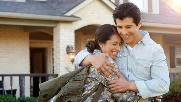 Mid-adult woman in uniform is pulled into hug by a mid-adult man. A smiling man pulls a smiling woman in uniform into a tight hug, while standing in front of home. mid adult men stock pictures, royalty-free photos & images