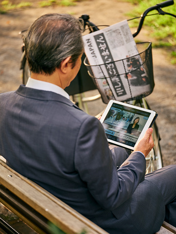 A mature Japanese man in a business suit watching online news in an outdoor setting in Tokyo, Japan.
