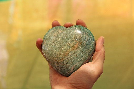 The hand holds the heart from a natural marble stone or green aventurine. Heart in hand. A stone in the shape of a heart. Love talisman, zen, spa.