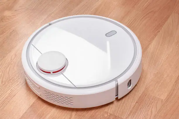 Photo of Robotic vacuum cleaner runs on laminate floor Closeup. modern smart cleaning technology housekeeping