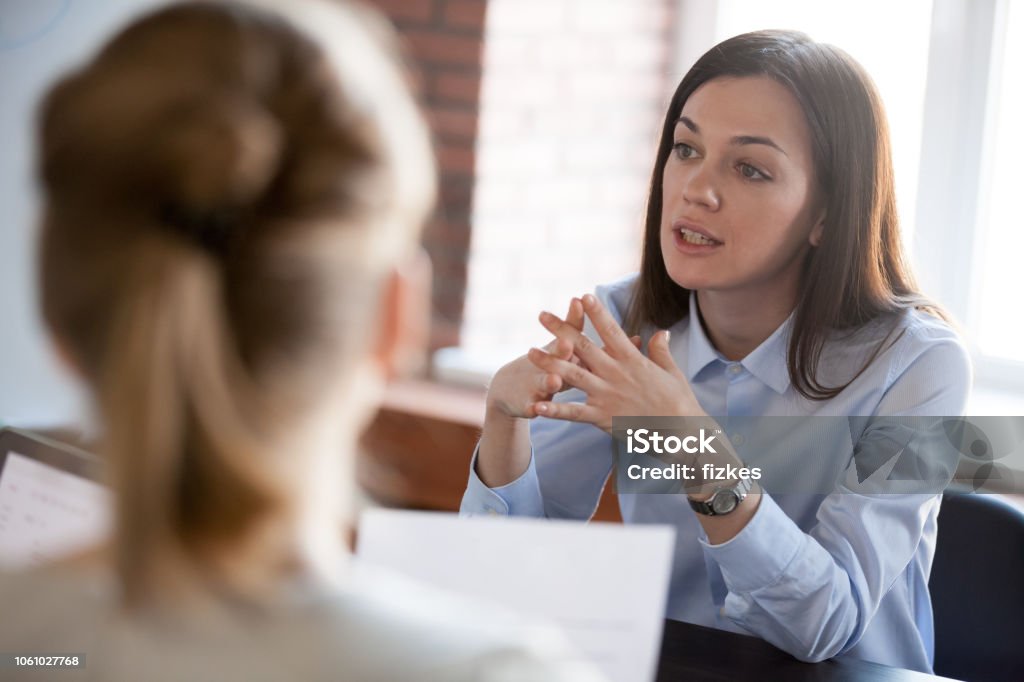 Confident focused businesswoman speaking to people at business negotiations Confident focused businesswoman, teacher or mentor coach speaking to business people at negotiations, woman leader speaker applicant talking at meeting or convincing hr during job interview concept Discussion Stock Photo