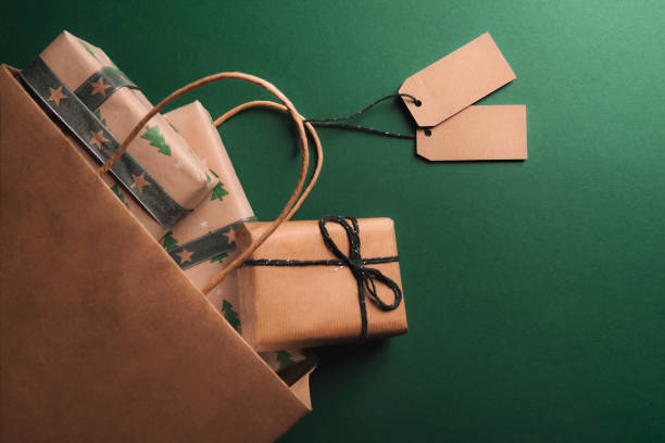 Overturned paper bag full of gifts Brown paper bag full of presents, with two empty tags, overturned on a green background, spreading gifts wrapped in classic paper. gift lounge stock pictures, royalty-free photos & images