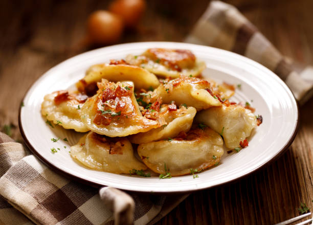 Fried dumplings stuffed with cabbage and meat sprinkled with bacon greaves and chopped parsley on a white plate Fried dumplings stuffed with cabbage and meat sprinkled with bacon greaves and chopped parsley on a white plate on a wooden rustic table. polish culture photos stock pictures, royalty-free photos & images