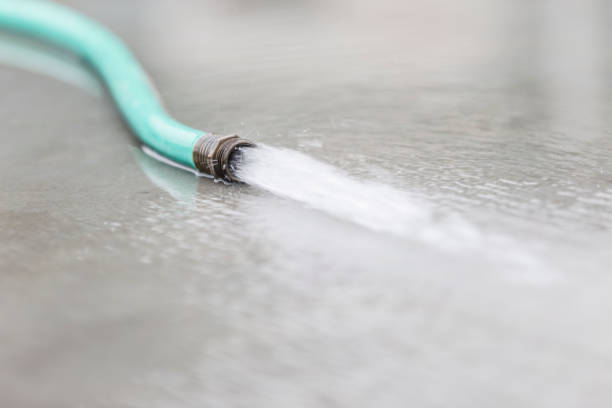 Green hose with little water coming out of the tube. Background cement wall.