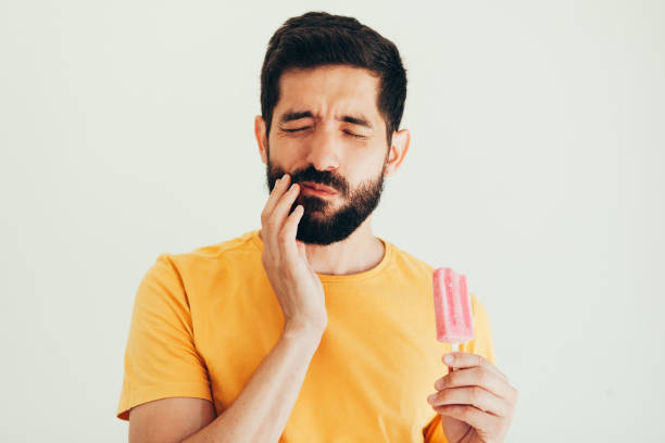 hombre tiene los dientes sensibles con hielo sobre fondo blanco - colmillo fotografías e imágenes de stock