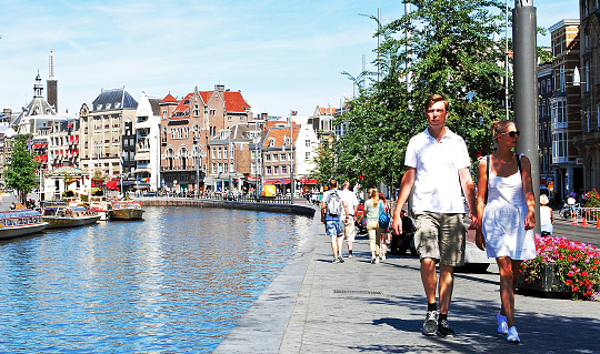 A young couple holding hands enjoying a relaxing walk along Rokin Street in Amsterdam during a sunny summer day.\