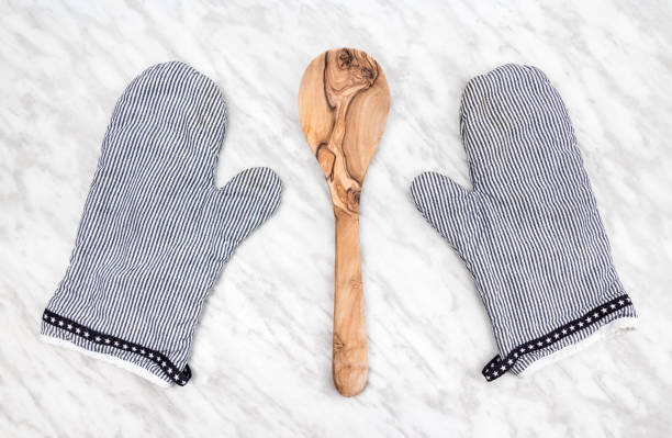 Wooden spoon and striped kitchen gloves, on a marble countertop.