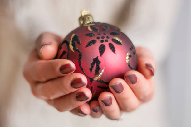 femmes mains avec manucure vernis à ongles brun tenant la boule de noël rouge - christmas ball christmas ornament human hand photos et images de collection