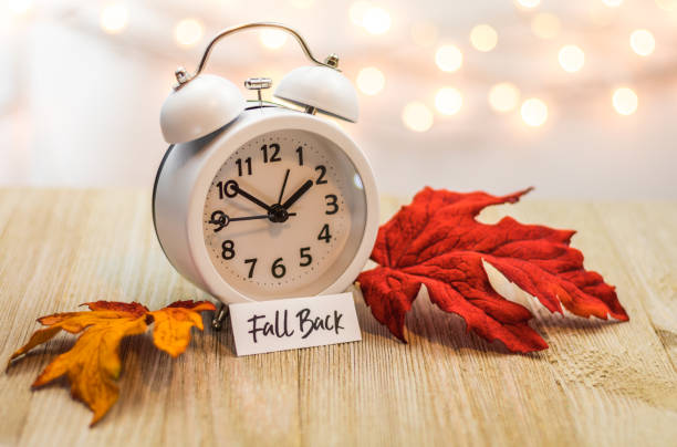 Fall Back Daylight Saving Time concept with white clock and autumn leaves stock photo