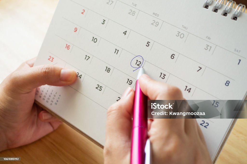 pagina del calendario con penna femmina che tiene la penna sul tavolo della scrivania - Foto stock royalty-free di Calendario