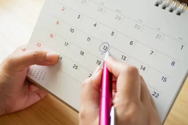 Photo of calendar page with female hand holding pen on desk table