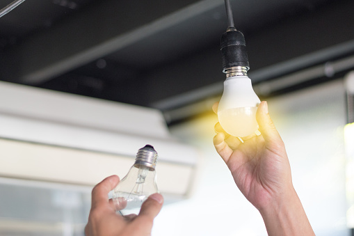 Concepto de ahorro de energía. Asia hombre cambiantes bulbos de fluorescente compacto (CFL) con la nueva bombilla LED de luz. photo