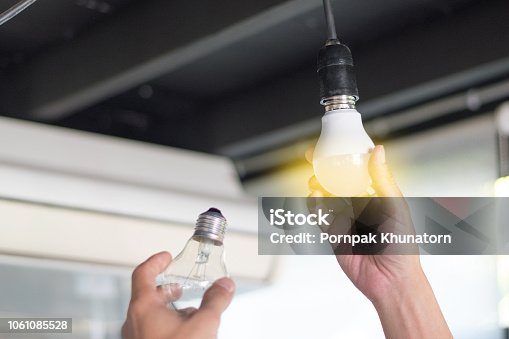 istock Power saving concept. Asia man changing compact-fluorescent (CFL) bulbs with new LED light bulb. 1061085528