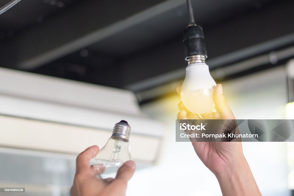 Conceito de economia de energia. Ásia o homem mudanças bulbos (CFL) de fluorescentes compactas com nova lâmpada de LED. - Foto de stock de Luz de LED royalty-free