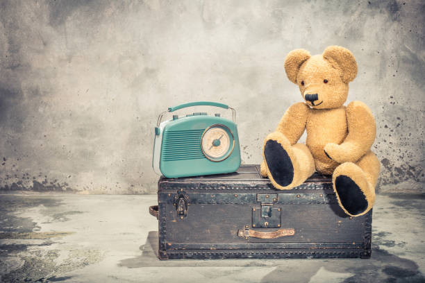 retro radio and teddy bear toy sitting on old aged classic travel trunk with leather handles circa 1900s. vintage instagram style filtered photo - radio 1930s imagens e fotografias de stock