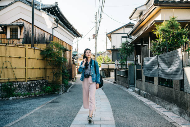 full length photo of an elegant lady walking in the path with Japanese traditional building around. Cheerful tourist travel in fun summer in Japan. Japanese lady going home.