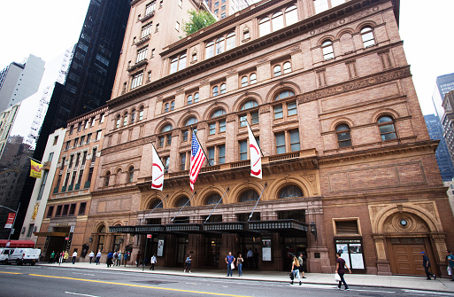 New York, NY: Carnegie Hall in midtown Manhattan, with pedestrians on the sidewalk outside. Wide angle shot.