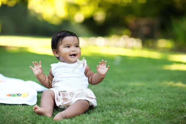 Happy baby girl sitting in the grass by herself and looking excited stock photo