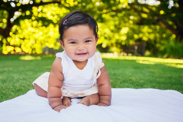 Adorable little baby girl with cute smile sitting unsupported and starting to take first crawling steps on her own, being independent and of mexican heritage. stock photo