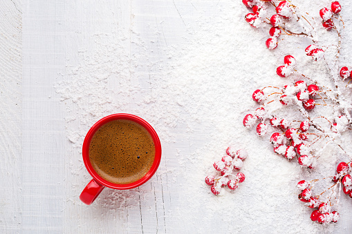 Red cup of coffee and branches with hawthorn berries on an old white wooden background. Flat lay.