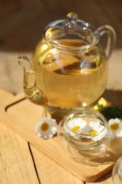 Chamomile tea.Tea in a teapots and a clear glass with fresh chamomile on a wooden board background.Healing natural herbs.Organic Pure Drink