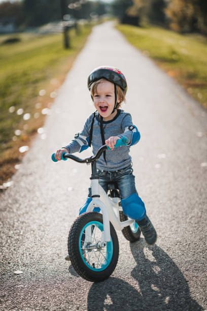 Cheerful little boy shouting while riding bicycle in the park. Happy small boy having fun on balance bicycle in nature. cycling helmet photos stock pictures, royalty-free photos & images